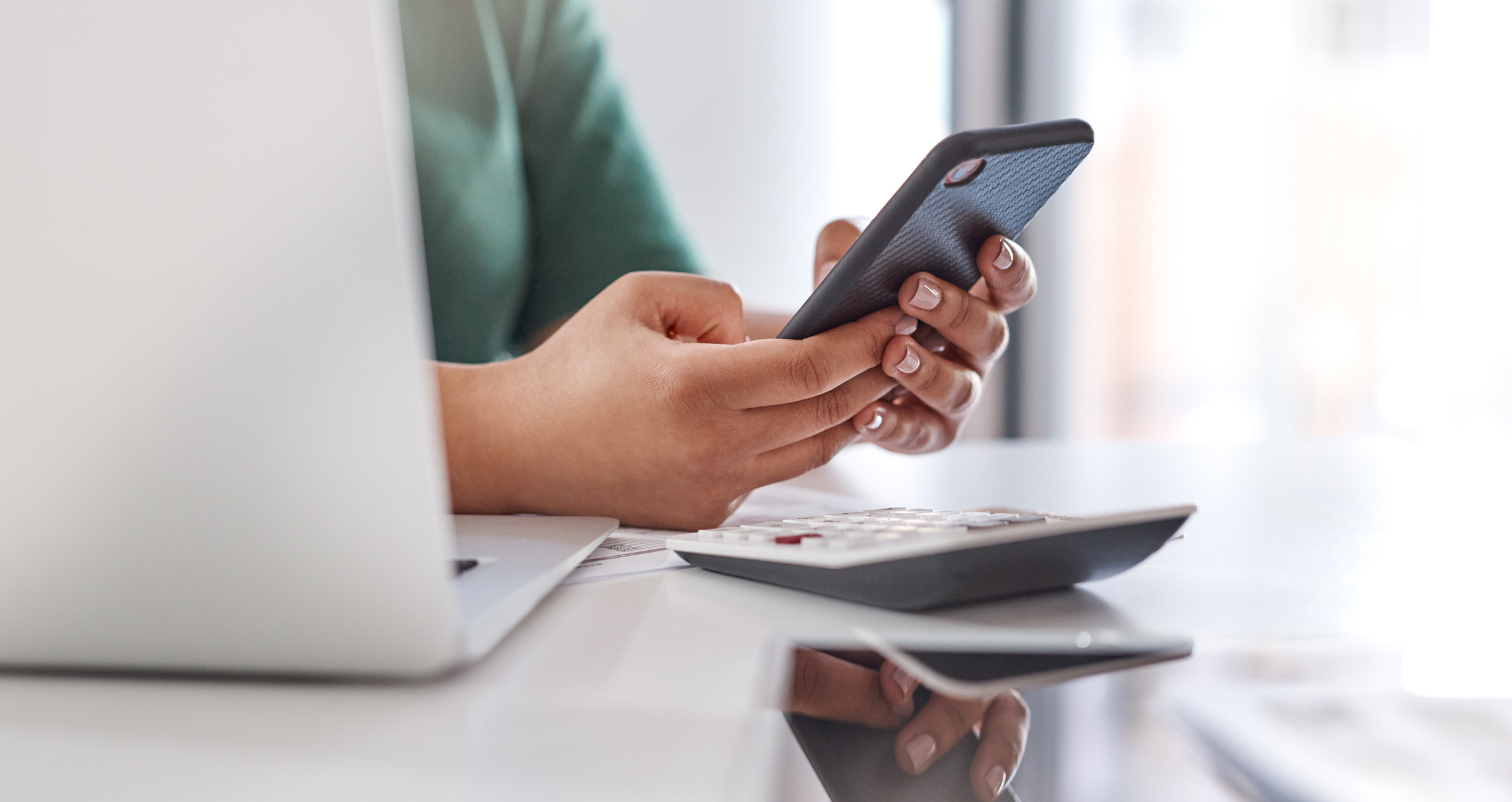 Shot of an unrecognisable woman using a smartphone and laptop at her desk